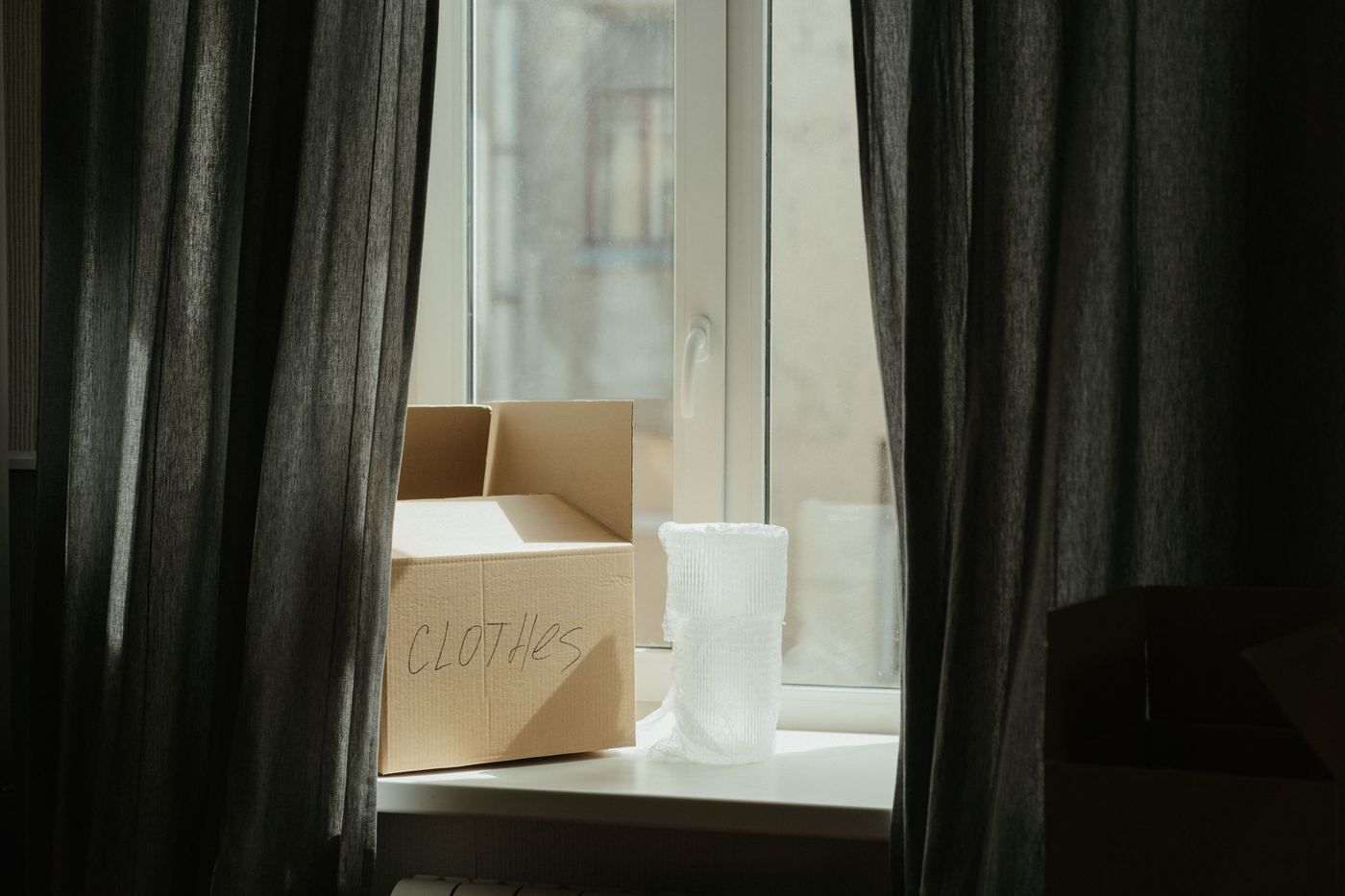 A single labeled moving box on a sunlit windowsill during a home transition